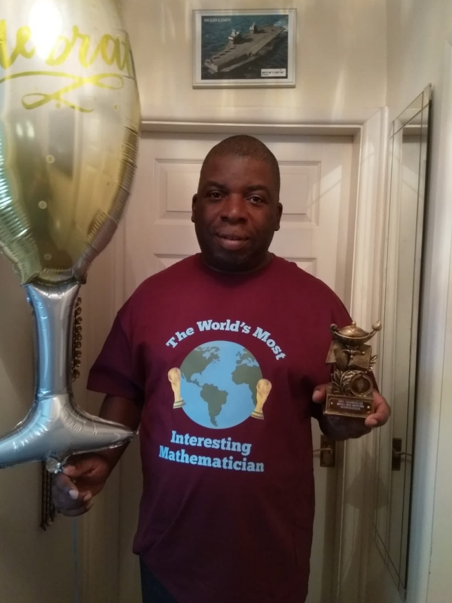 Photo of Nira Chamberlain holding a trophy and wearing a t-shirt saying "world's most interesting mathematician"